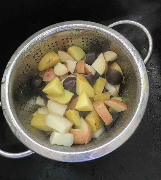 Recently boiled potatoes in all different colors sitting in a strainer cooling off and waiting to be added to the dressing.