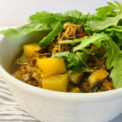 bowl of soup with potatoes, shredded pork, chayote squash and peppers topped with peppery arugula